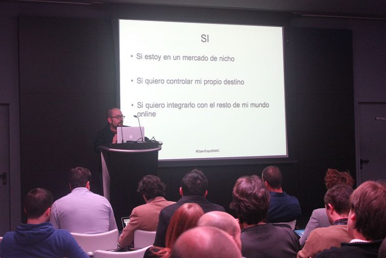 Dani Primo en el atril dando una charla en OpenExpo SMAC Madrid, con el público de espaldas y una diapositiva proyectada detrás